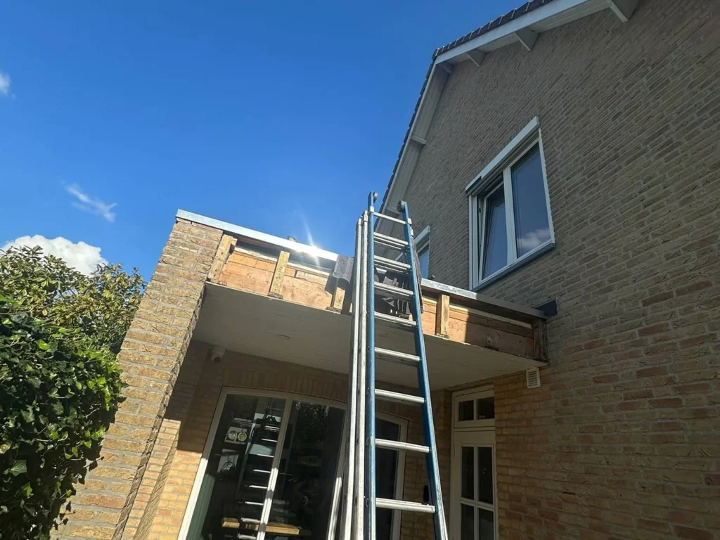 Opengewerkte dakrand van een aanbouw met ladder tegen de gevel in Barneveld