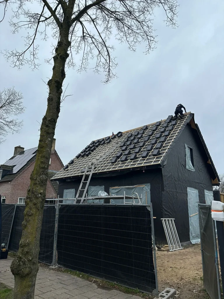 Dakdekker legt dakpannen op een hellend dak achter bouwhekken in Barneveld