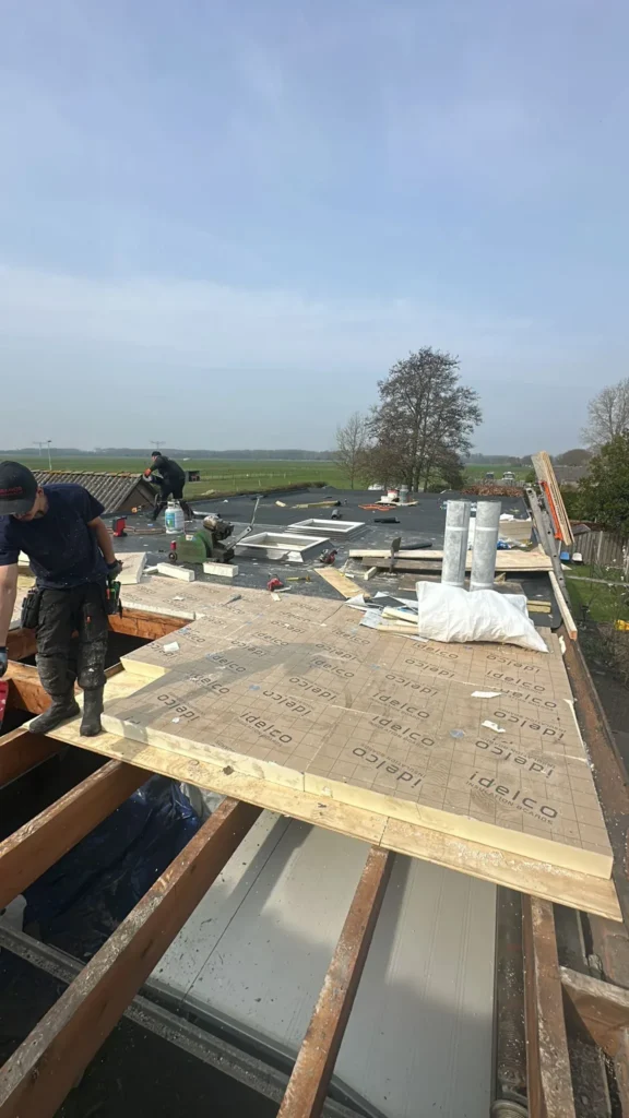 Dakdekkers leggen nieuw dakbeschot op de balken van een plat dak in Barneveld