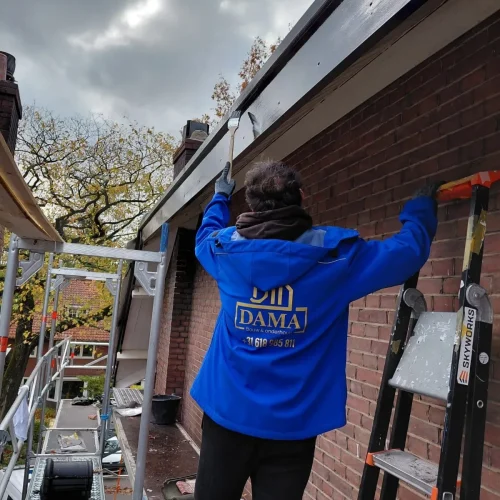 Dakdekker op een trap werkt aan de dakrand van een bakstenen woning in Barneveld