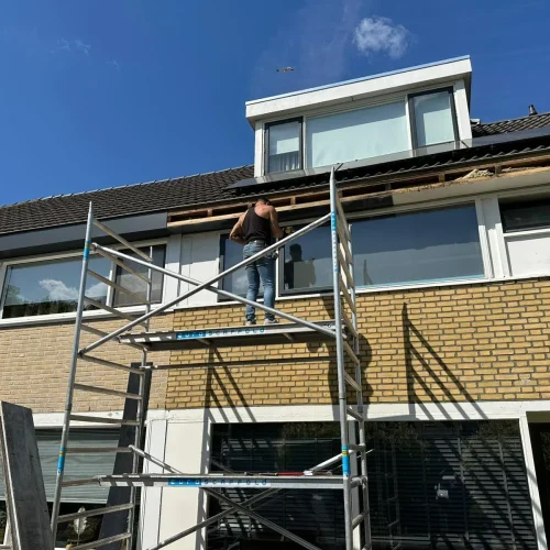 Vakman op een rolsteiger werkt aan de dakvoet van een rijtjeshuis met dakkapel in Lunteren